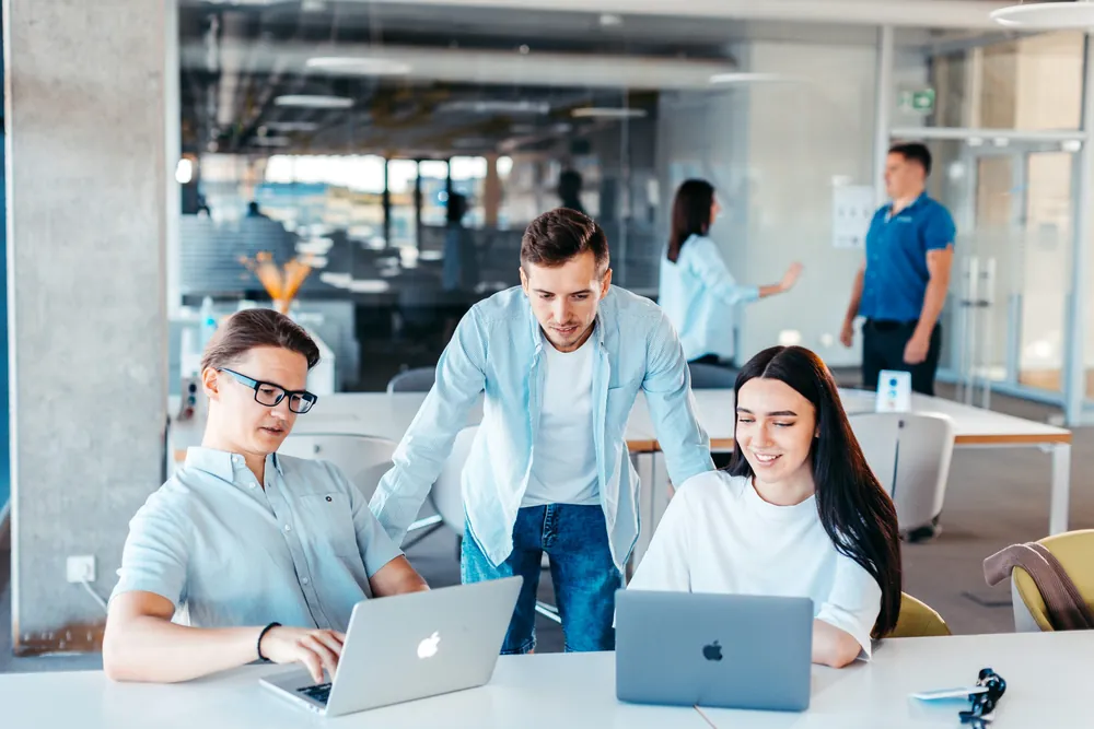 Young founders discussing a startup build plan around laptops in a modern office, representing the decision point of when to bring in a real engineer